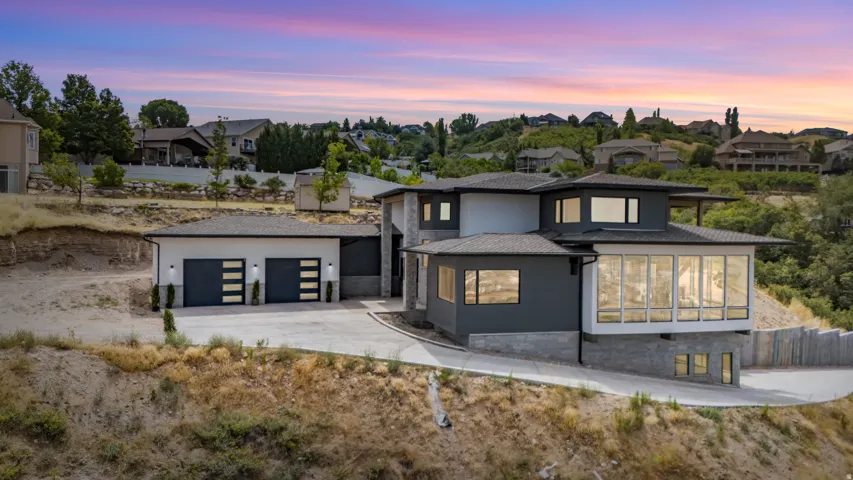 Modern architectural residence featuring multi-level design, a two-car garage with contemporary doors, extensive floor-to-ceiling windows, a stone-clad foundation, and a sloped concrete driveway