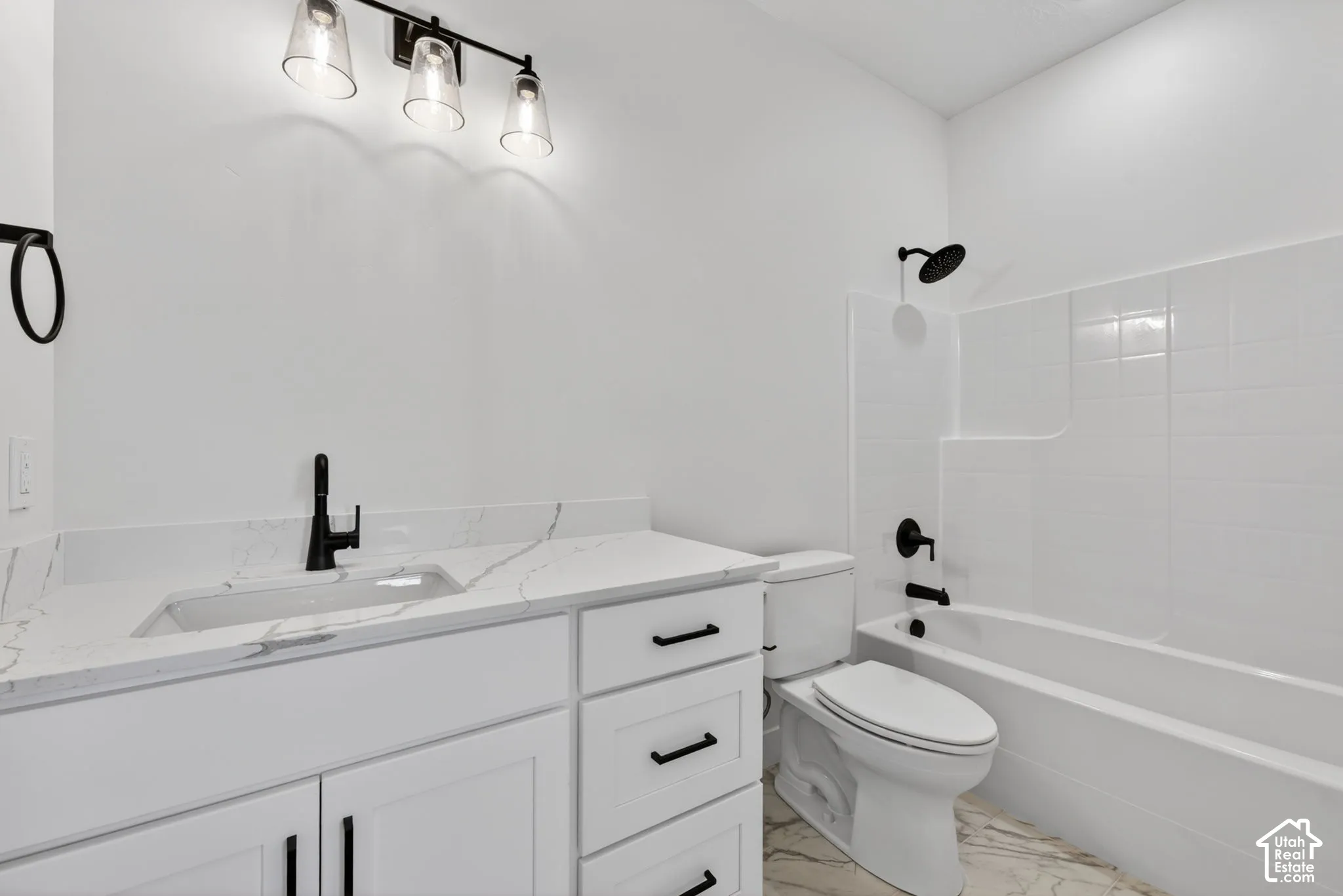 Bathroom featuring a white vanity with a stone-finish countertop, matte black fixtures, a built-in tub with white subway tile surround, and a three-light vanity fixture