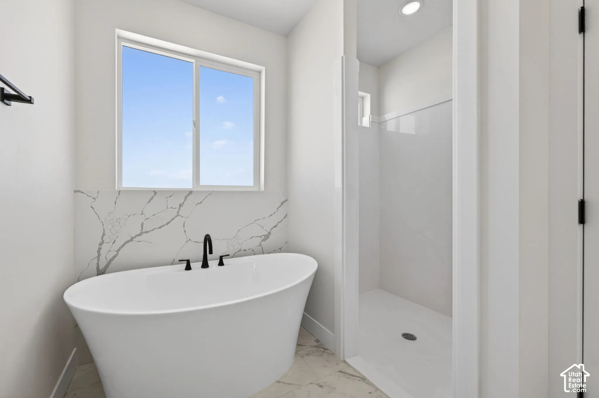 Freestanding soaking tub with matte black fixtures set against a large-format veined accent wall and a window