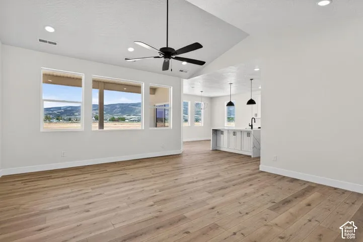 Open-concept interior featuring vaulted ceilings, wood-finish flooring, a matte black ceiling fan, recessed lighting, and a kitchen island with pendant lighting
