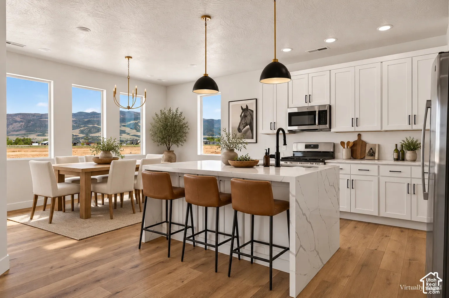 Kitchen featuring white shaker-style cabinetry, quartz waterfall island, wood-finish flooring, stainless steel appliances, and matte black hardware