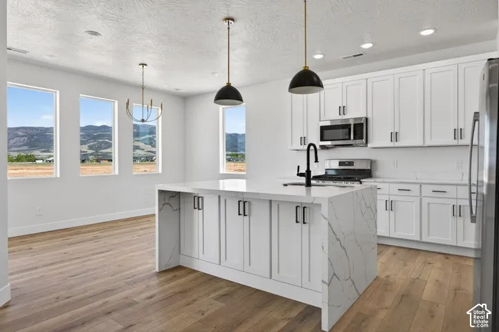Kitchen featuring a waterfall-edge island with stone-finish countertop, white cabinetry, wood-finish flooring, matte black hardware, and pendant lighting