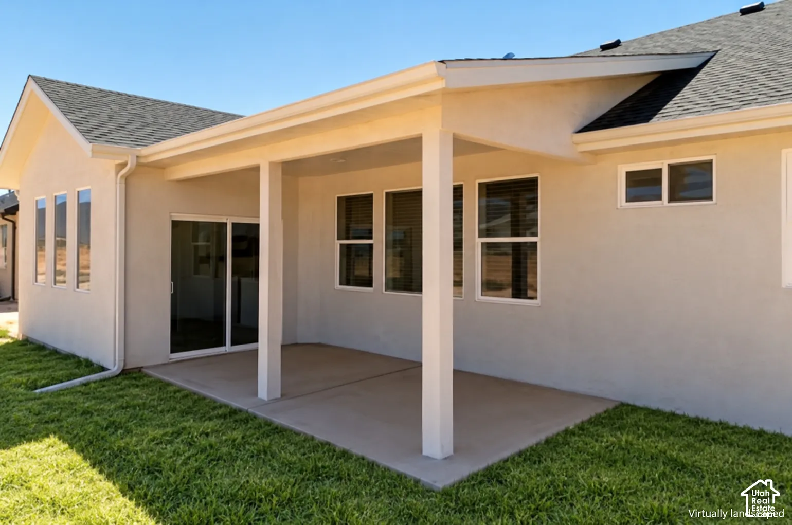Covered concrete patio featuring a stucco exterior, shingle roof, sliding glass door, and multiple windows