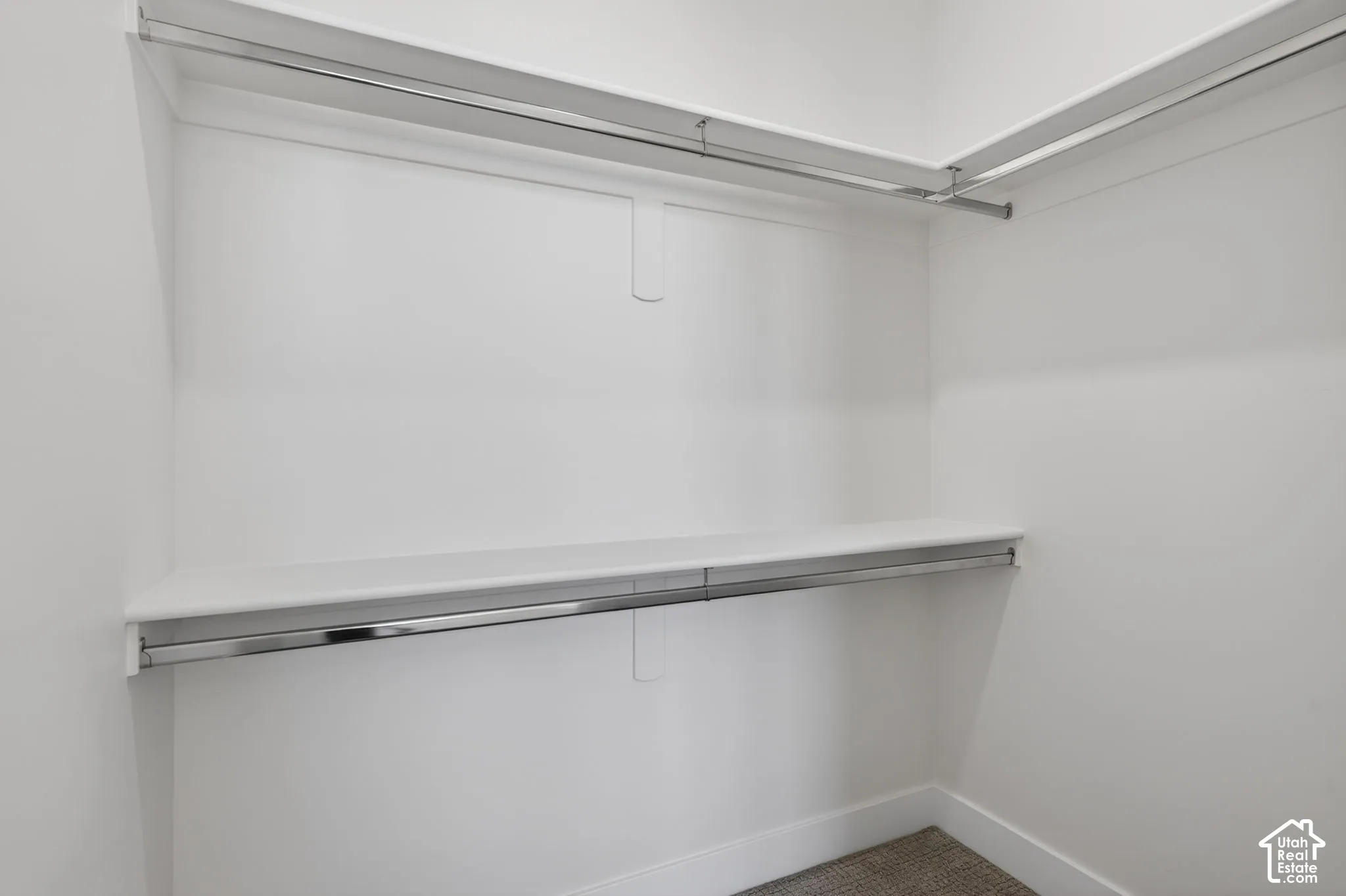 Walk-in closet featuring white walls, white shelving, polished chrome hanging rods, and neutral-toned carpet flooring