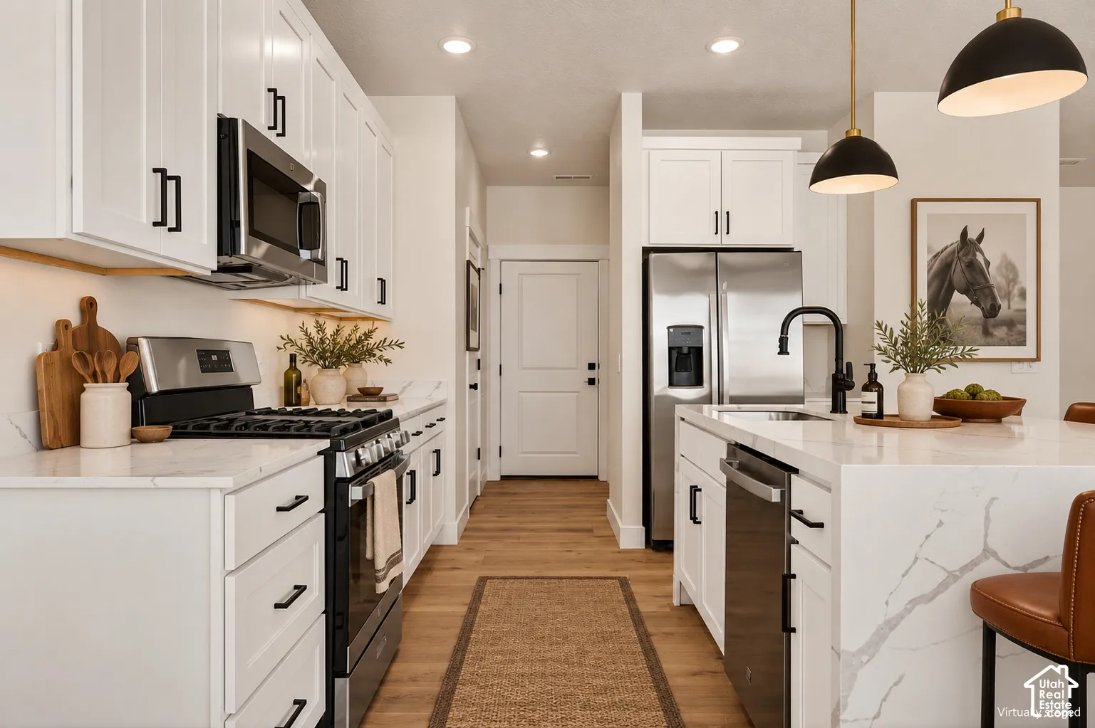 Kitchen featuring white cabinetry with matte black hardware, quartz countertops, stainless steel appliances, wood-finish flooring, and pendant lighting