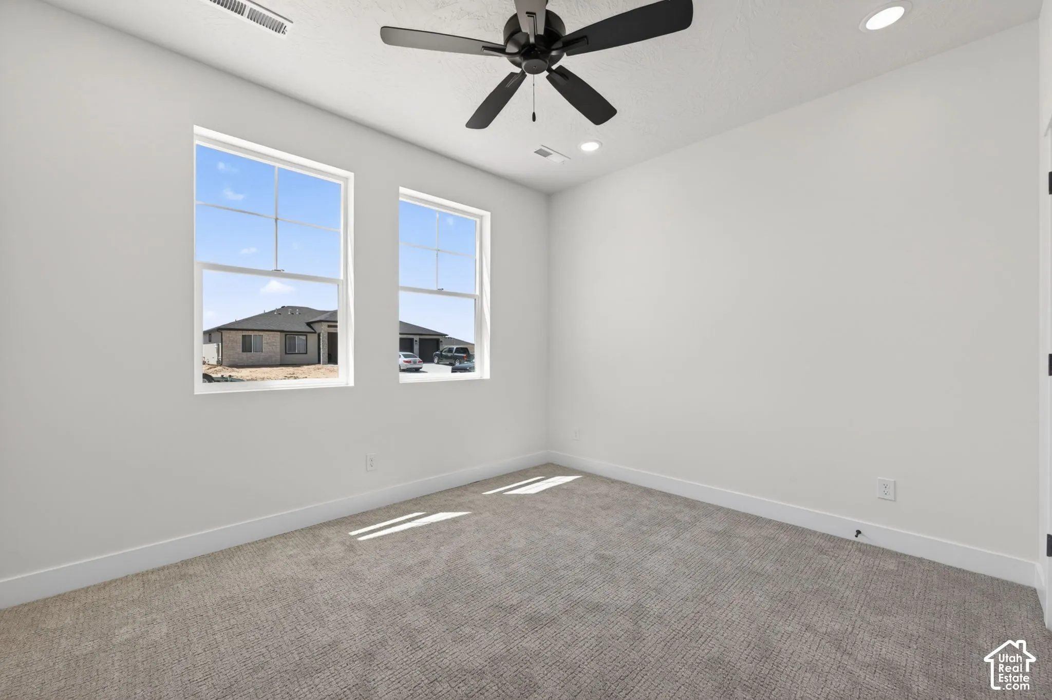 Spacious room featuring two large windows, a ceiling fan with integrated lighting, and recessed lighting fixtures
