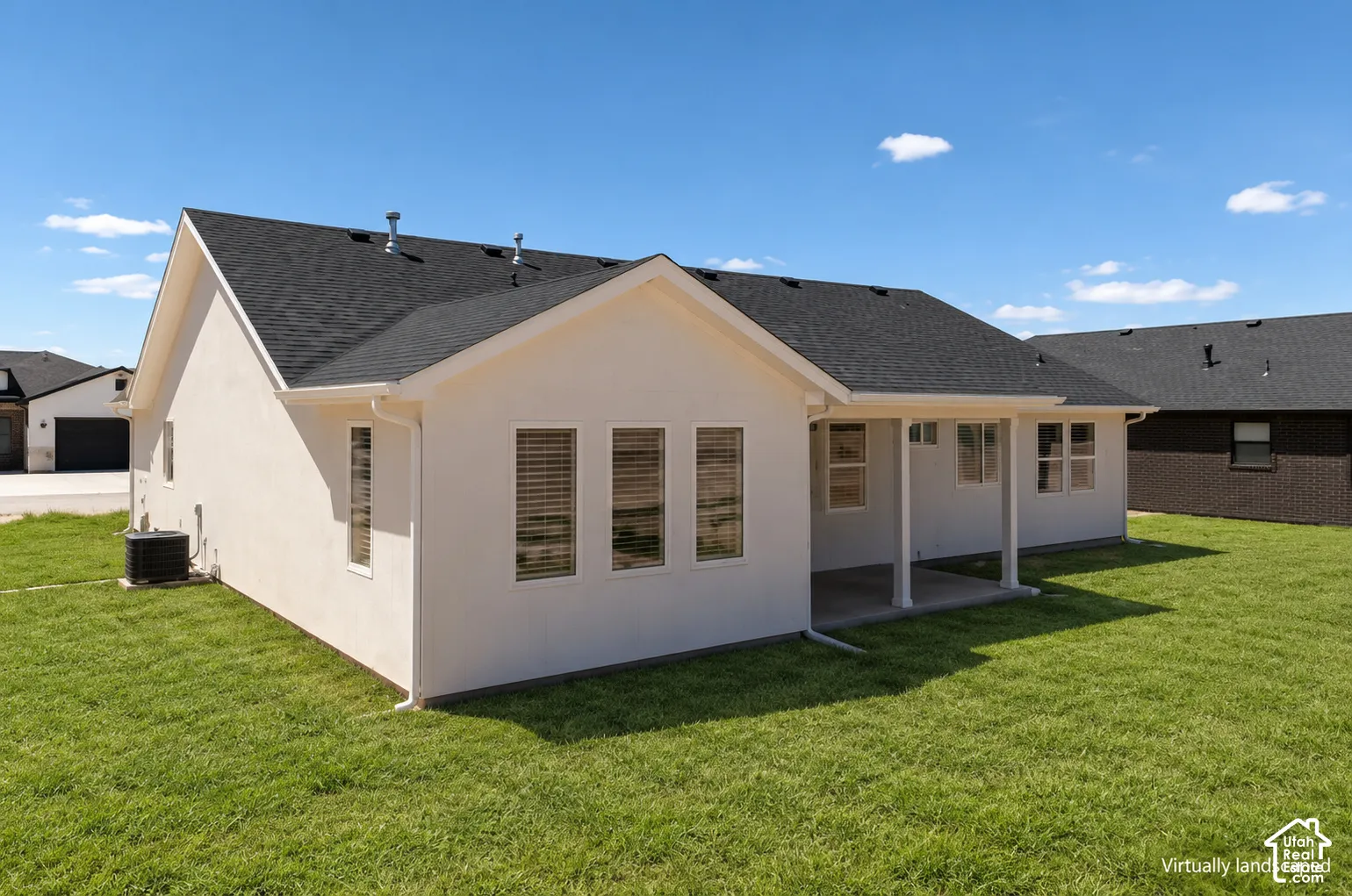 Exterior featuring a light-toned stucco finish, an asphalt shingle roof, a covered patio with support columns, and an expansive lawn
