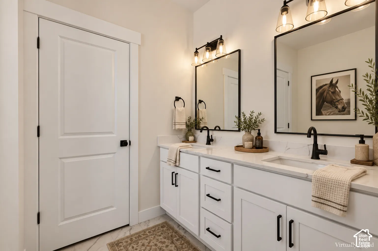 Dual-sink vanity with white cabinetry, stone-finish countertops, matte black hardware, and two framed mirrors with matching wall-mounted light fixtures