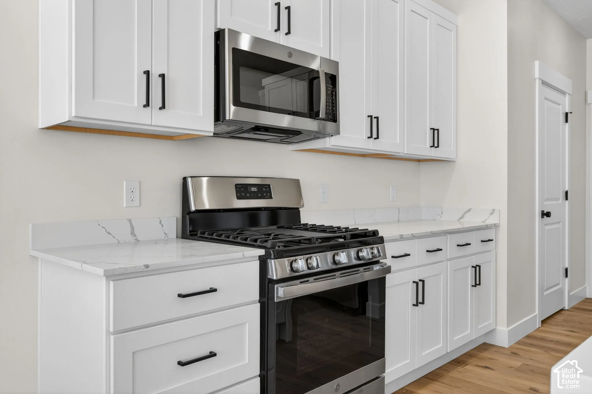 Kitchen featuring white shaker-style cabinetry, stainless steel appliances, and wood-finish flooring