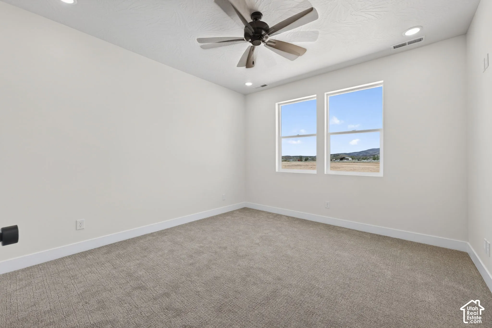 Spacious room featuring neutral carpeting, white baseboards, and a modern ceiling fan