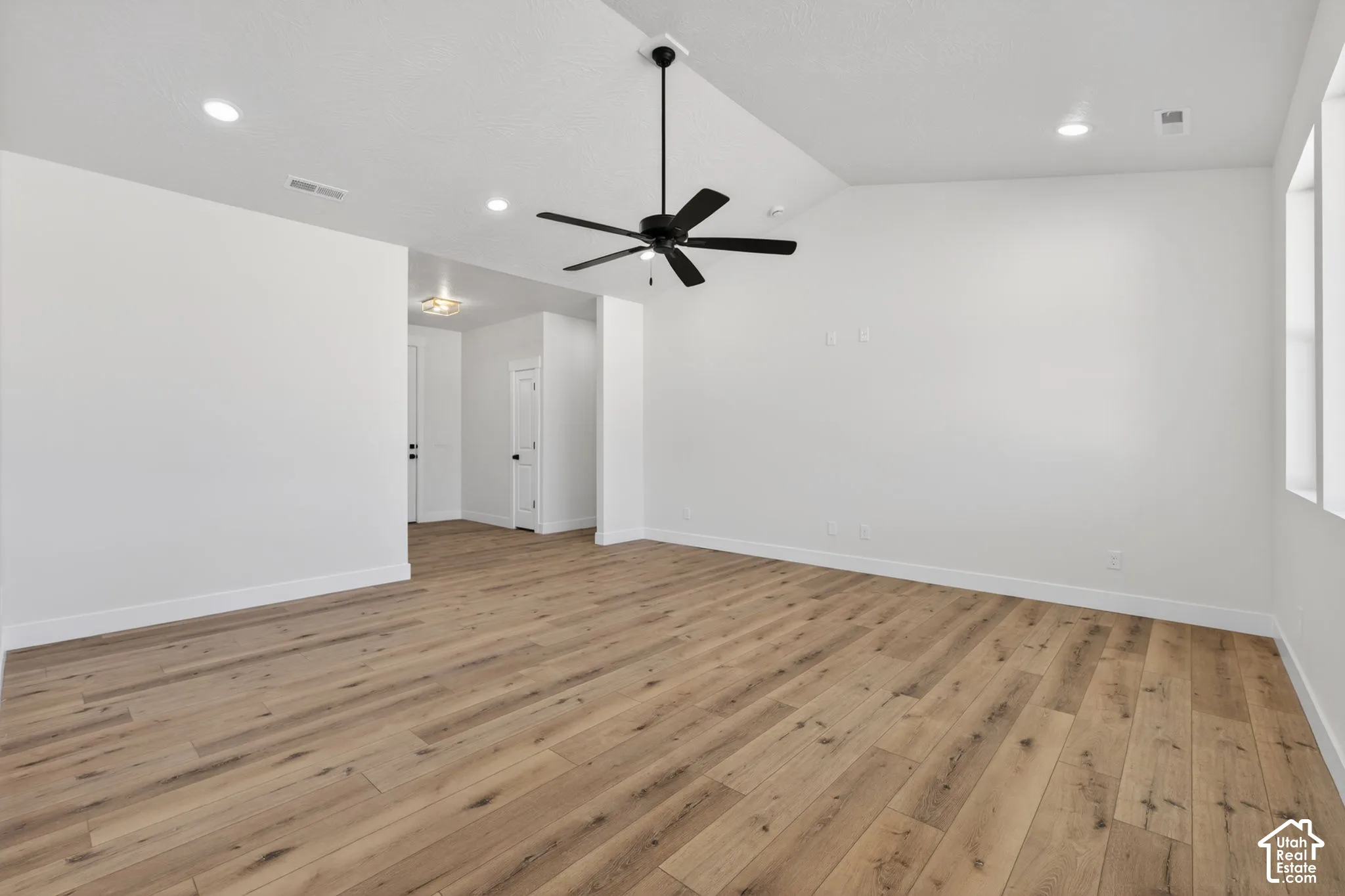 Spacious room featuring wood-finish flooring, high ceilings with a modern ceiling fan, recessed lighting, and multiple windows