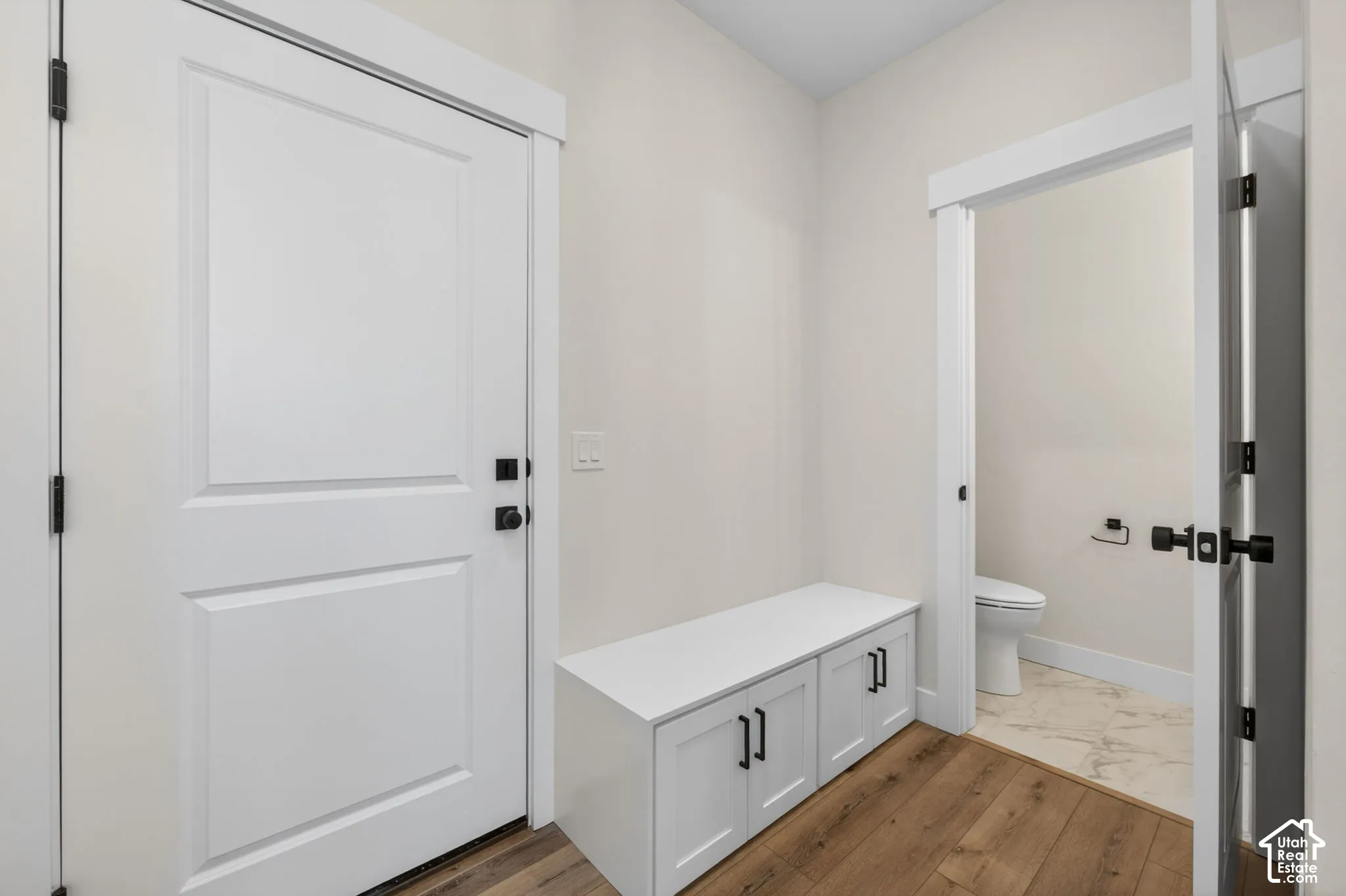 Entryway featuring wood-finish flooring, a built-in storage bench with cabinet doors and black hardware, and a white paneled door with black hardware