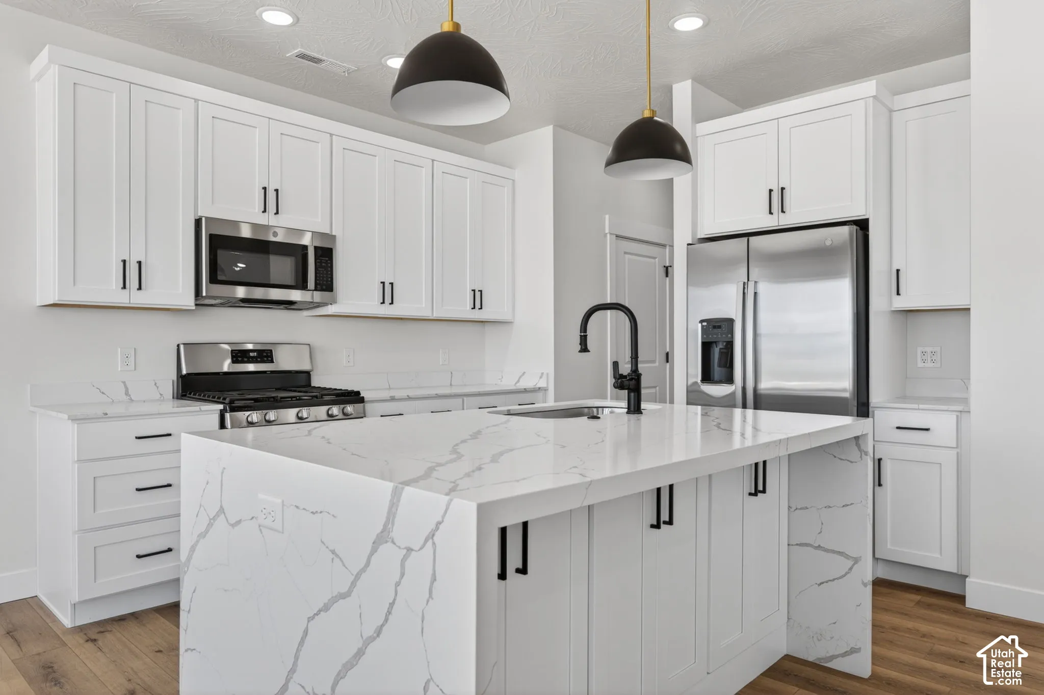 Modern kitchen featuring white shaker cabinetry, stainless steel appliances, a center island with waterfall edge countertop, and wood-finish flooring