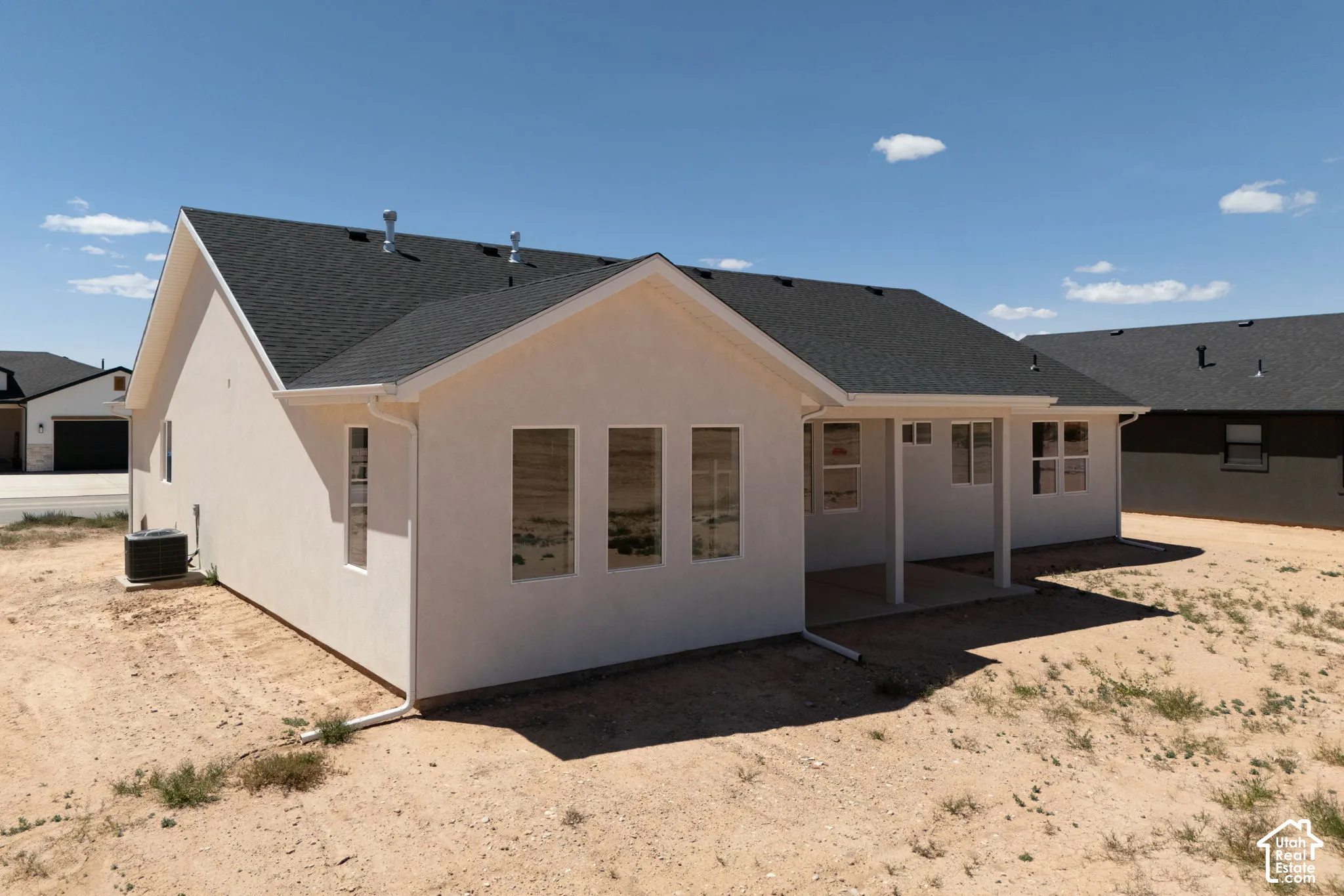 Contemporary exterior featuring light-colored stucco, a dark shingle roof, and multiple windows
