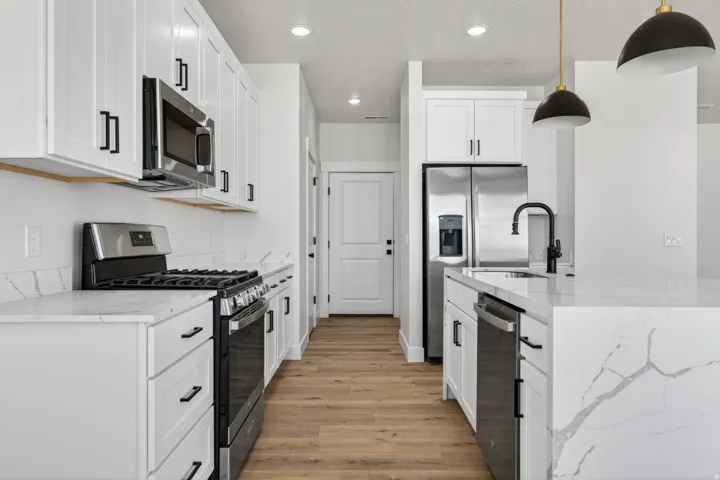 Modern kitchen featuring white cabinetry with matte black hardware, stainless steel appliances, wood-finish flooring, white countertops with veining, and a kitchen island with pendant lighting