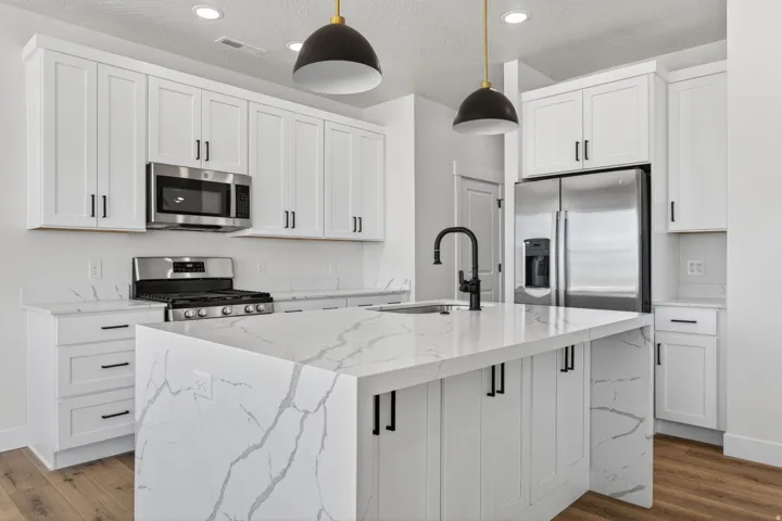 Modern kitchen featuring white shaker cabinetry, stainless steel appliances, a center island with waterfall edge countertop, and wood-finish flooring