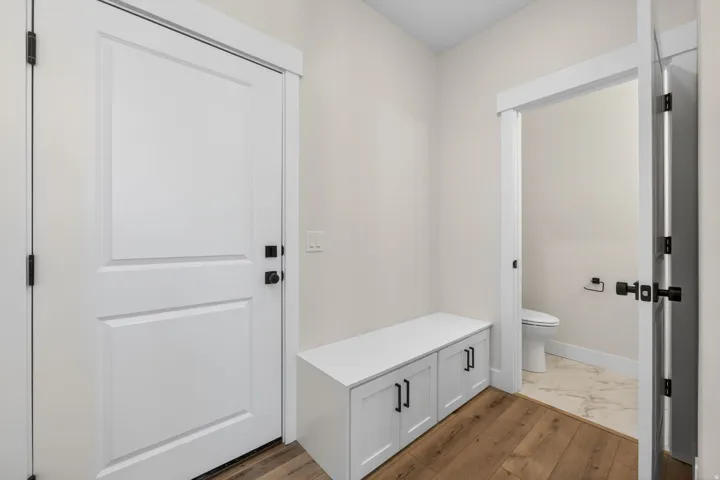 Entryway featuring wood-finish flooring, a built-in storage bench with cabinet doors and black hardware, and a white paneled door with black hardware