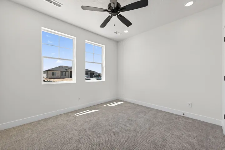 Spacious room featuring two large windows, a ceiling fan with integrated lighting, and recessed lighting fixtures