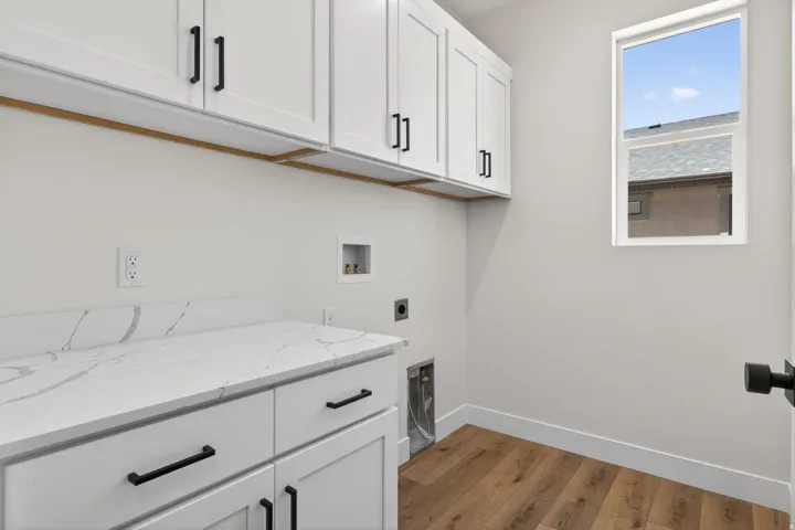 Laundry area featuring white shaker-style cabinetry with matte black hardware, a light-colored countertop with veining, and wood-finish flooring