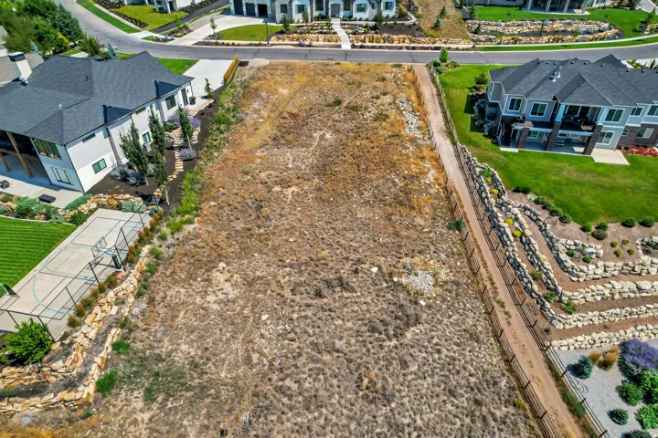 Expansive, undeveloped parcel featuring natural ground cover, bordered by established properties with manicured lawns and rock retaining walls