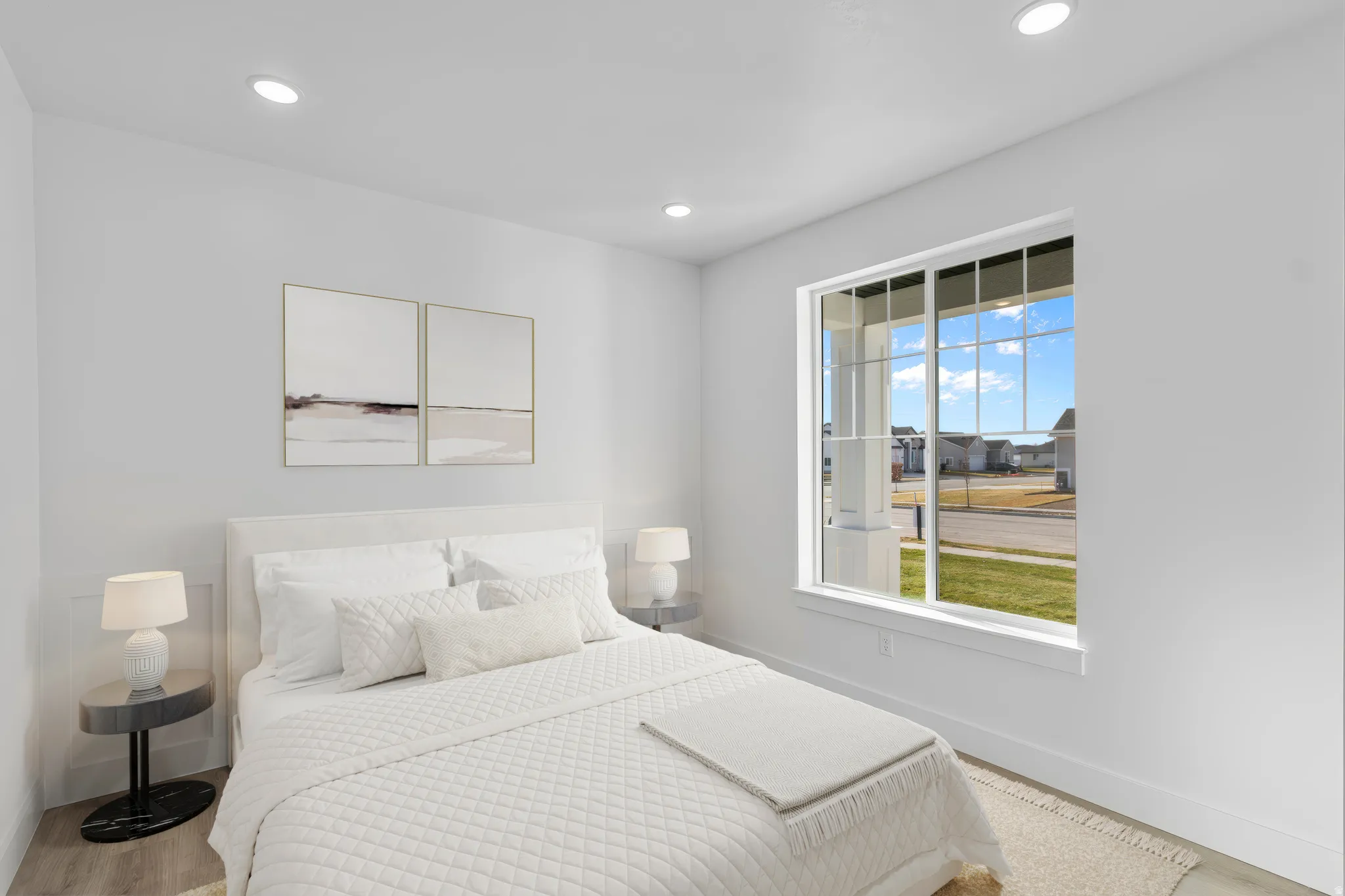 Bright secondary bedroom featuring a white quilted bedside table, recessed ceiling lighting, and large picture window with expansive outdoor scenery