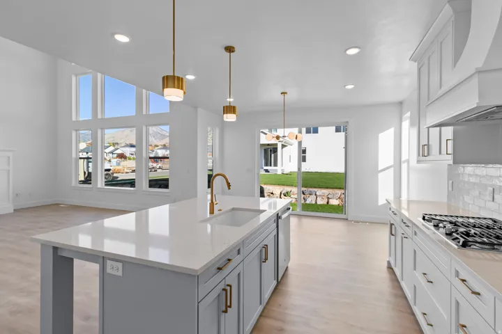 Bright, modern kitchen showcasing a large gray center island with white quartz countertop, stainless steel gas cooktop, and brass pendant lighting