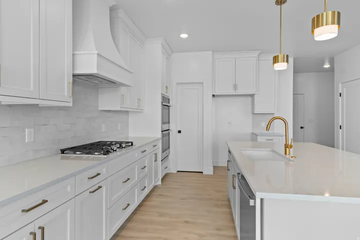 Chef's kitchen featuring white cabinetry with brass hardware, a gas cooktop with stainless steel hood, quartz countertops, a large waterfall-edge island with seating, pendant lighting with brass accents, subway tile backsplash, and wood-finish flooring th