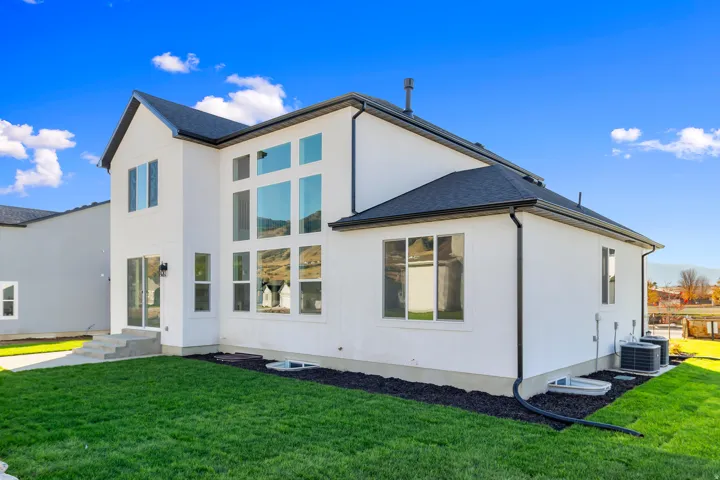 Modern farmhouse exterior showcasing a crisp white facade with black roof accents, expansive multi-pane windows flooding interiors with natural light, two-story architectural design with gabled rooflines, manicured lawn with defined landscaping borders, a