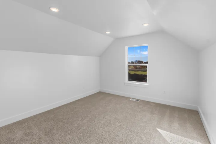 Bright upper-level bedroom with vaulted ceilings, recessed lighting, and neutral carpet flooring
