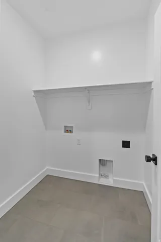 Dedicated laundry area featuring a white wall shelf, gray tile flooring, and white baseboards
