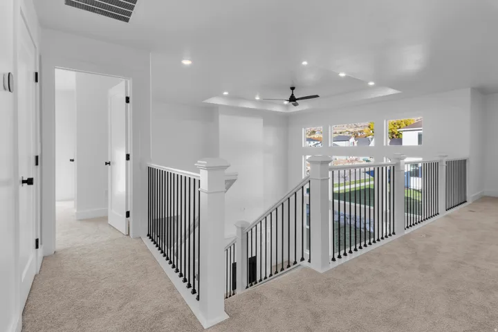 Spacious upper-level landing featuring elegant black metal railings, recessed ceiling lighting, and neutral carpet flooring