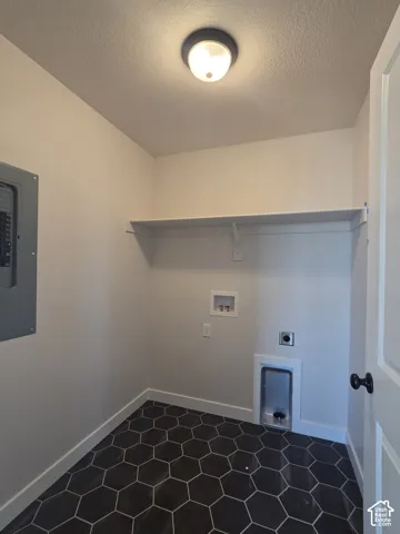 Utility room featuring dark hexagonal floor tile, built-in overhead shelving, electrical panel, and dedicated plumbing hookups