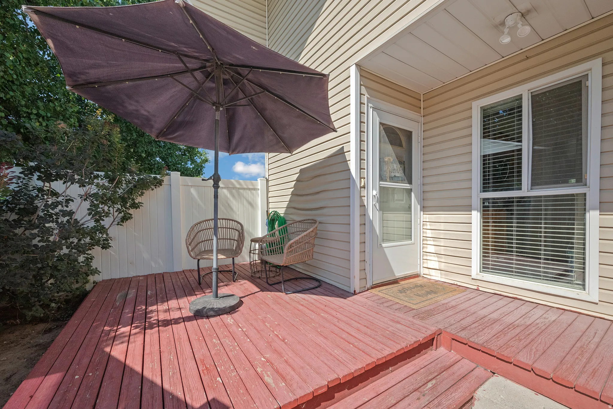 Red-stained wooden deck featuring steps and a white privacy fence