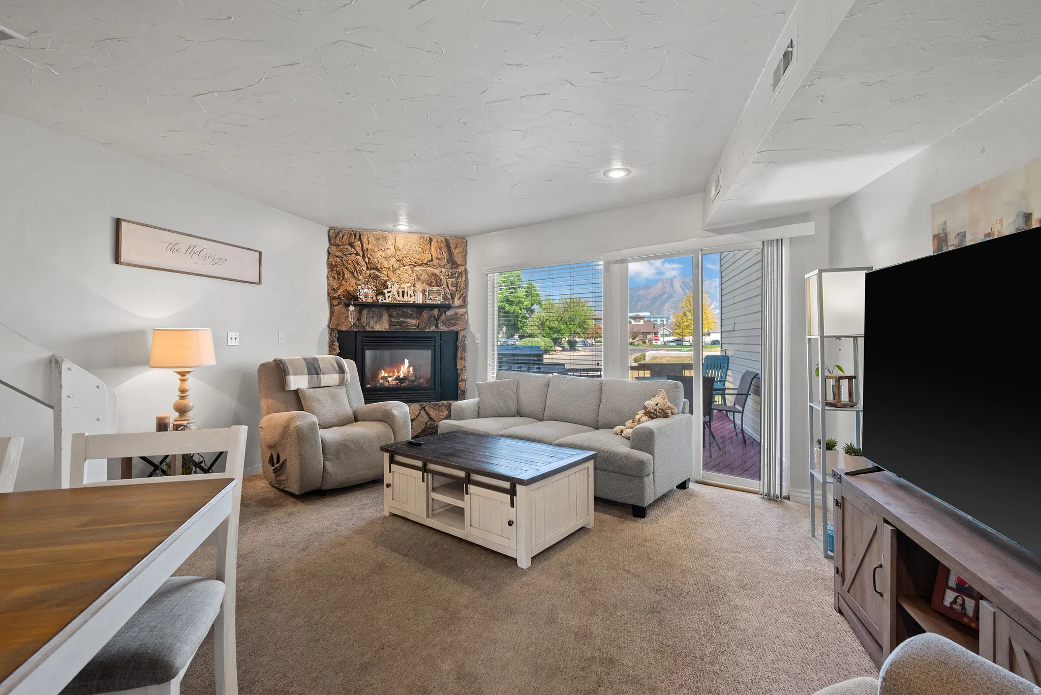 Living area featuring a stone-clad corner fireplace, sliding glass door access to an exterior space, and light-colored carpeting