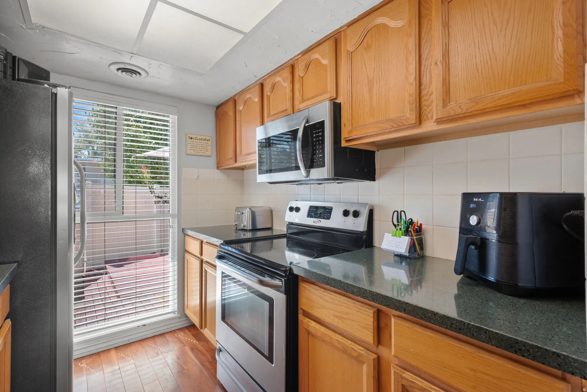 Kitchen featuring wood-finish cabinetry, dark countertops, a tile backsplash, stainless steel appliances, and wood-finish flooring