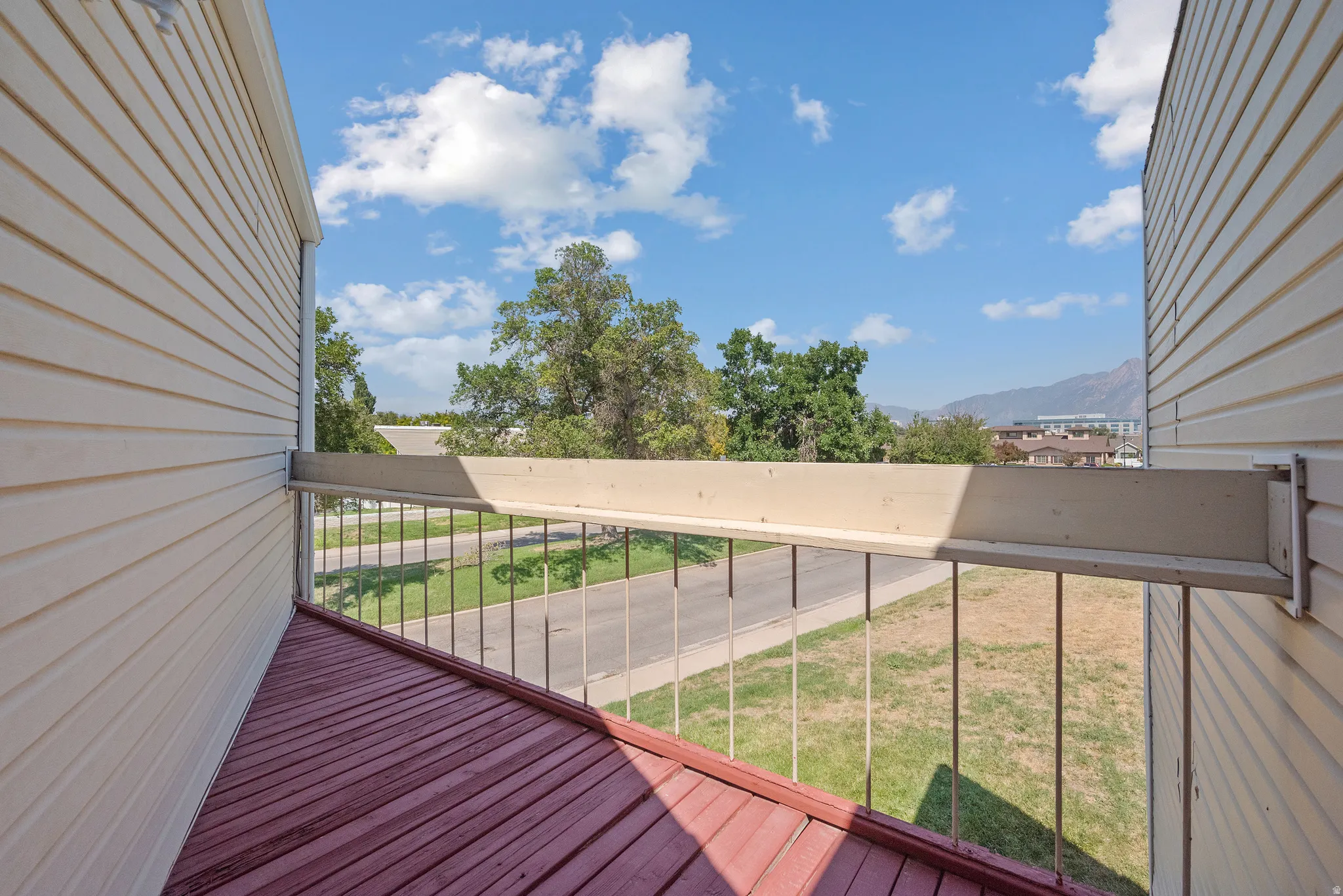 Outdoor balcony featuring a red-toned plank flooring, metal railings, and a partial mountain backdrop