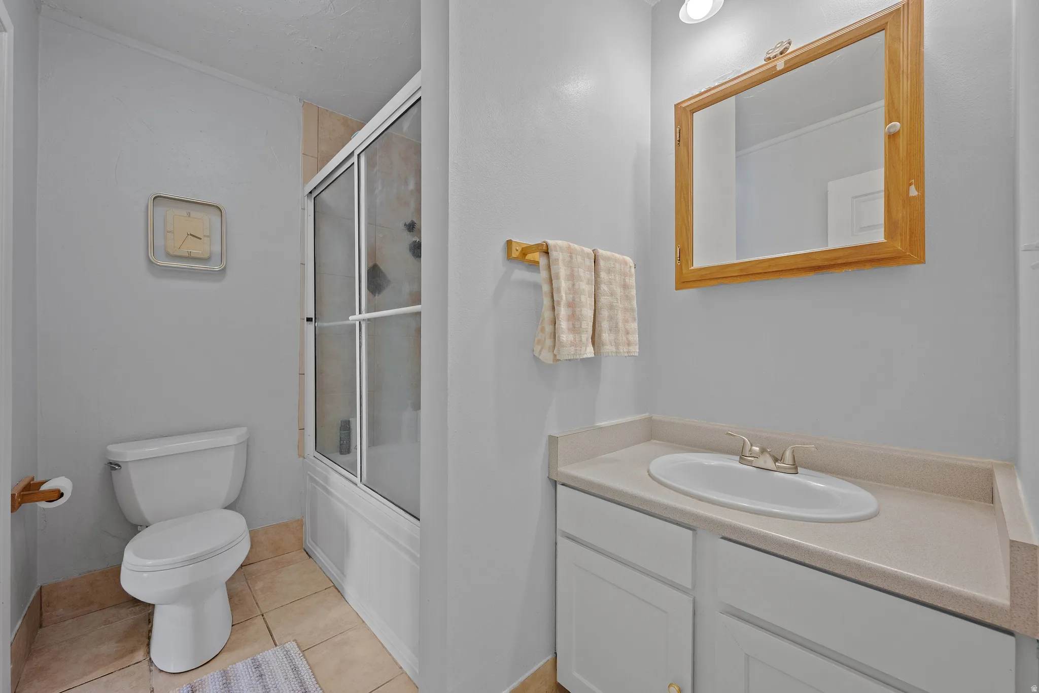 Bathroom featuring a tub/shower combination with sliding glass doors, a vanity with a light-toned countertop, a built-in sink, and a framed mirror