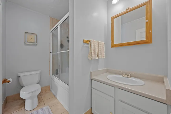Bathroom featuring a tub/shower combination with sliding glass doors, a vanity with a light-toned countertop, a built-in sink, and a framed mirror
