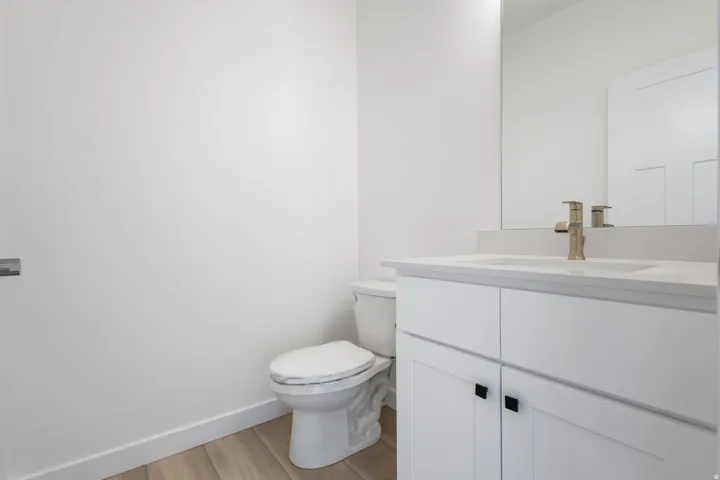Bathroom featuring wood-finish flooring, a white vanity with black hardware, a light-colored countertop, and a brushed nickel faucet