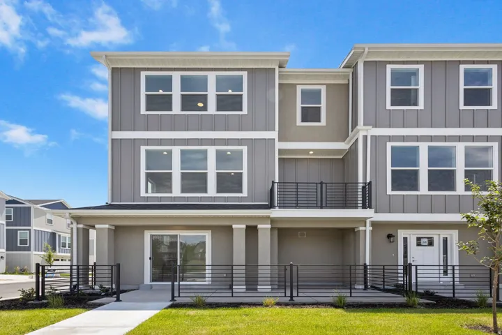Contemporary townhome exterior featuring multi-level architecture, a private balcony with black metal railing, and a covered patio