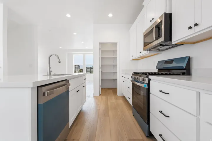 Modern kitchen featuring wood-finish flooring, white cabinetry with matte black hardware, stainless steel appliances, and a walk-in pantry