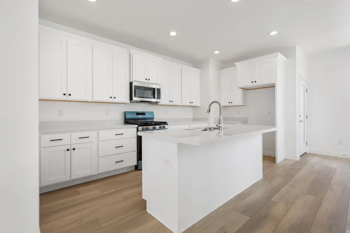 Modern kitchen featuring white shaker cabinetry, light-toned countertops, and wood-finish flooring