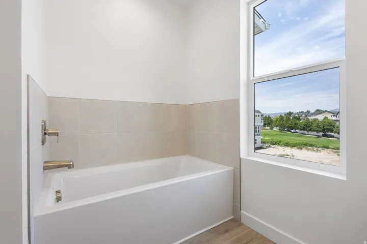 Soaking tub with brushed nickel fixtures, light-toned wall tiles, and wood-finish flooring