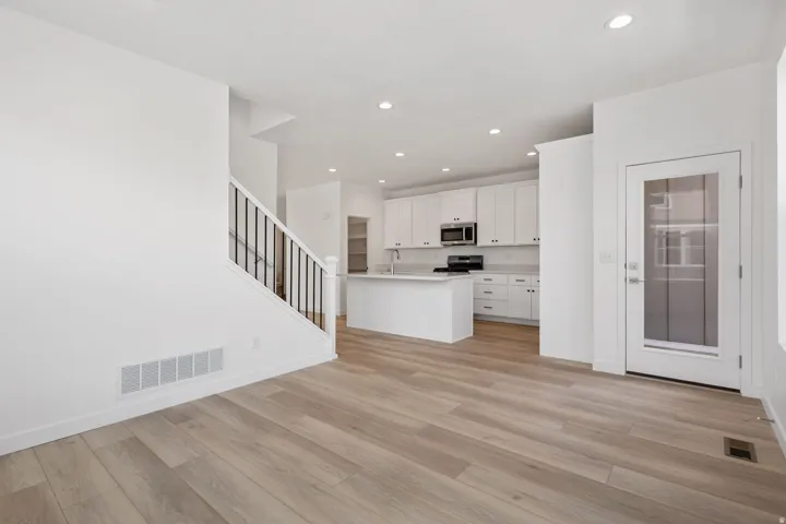 Open-concept living space featuring wood-finish flooring, a white kitchen with stainless steel appliances, a kitchen island, white cabinetry, and recessed lighting