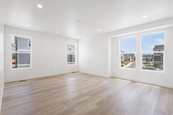 Spacious room featuring light wood-finish flooring, recessed lighting, multiple windows, and crisp white walls