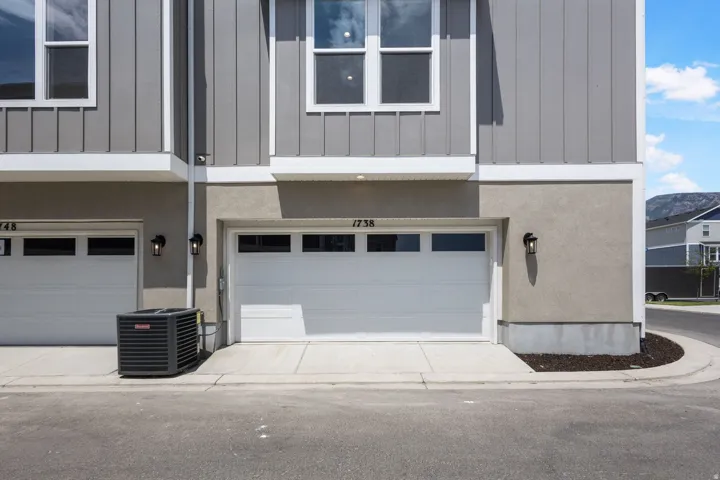 Modern townhome exterior featuring a white garage door with upper window inserts, gray vertical siding, and a stucco finish