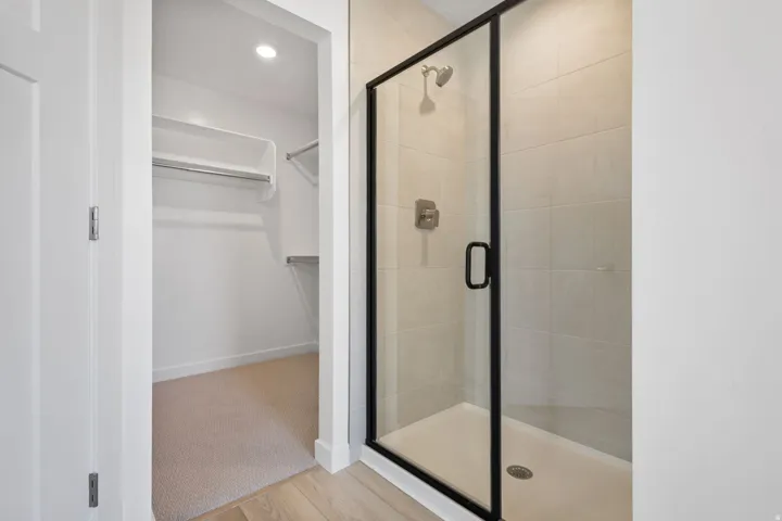 Walk-in closet with carpeted flooring and recessed lighting, accompanied by a glass-enclosed shower featuring tiled walls and a brushed nickel showerhead