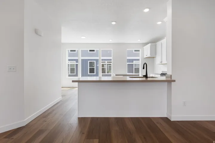 Open-concept kitchen featuring an eat-at counter, light-toned countertops, white cabinetry, a black gooseneck faucet, and recessed lighting