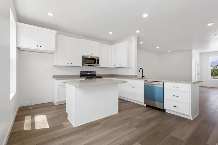 Modern kitchen featuring white cabinetry, light countertops, wood-finish flooring, a central island, and stainless steel appliances