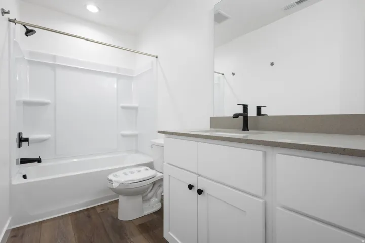 Bathroom featuring a white tub/shower combination, dark wood-finish flooring, a white vanity with slab countertop, and contemporary black fixtures